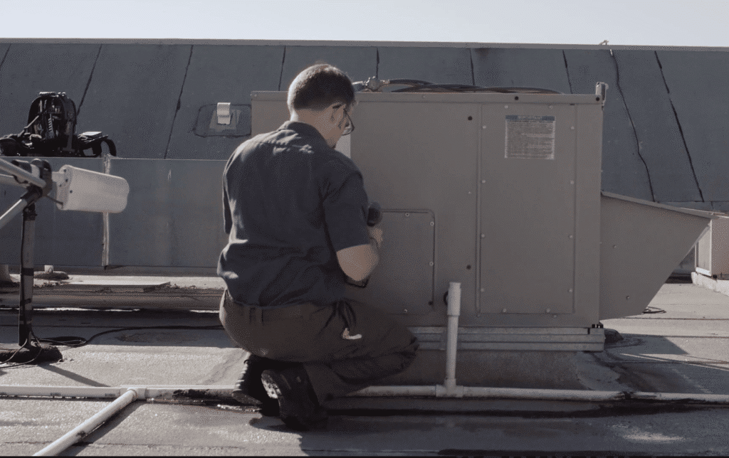 Video still of a technician kneeling by a rooftop hvac unit