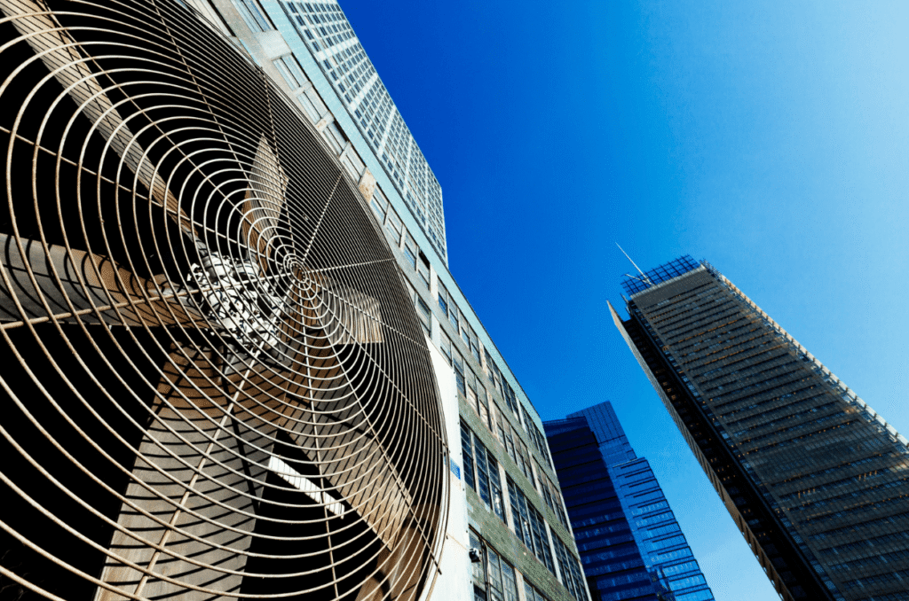 Looking up at a large industrial fan on a building beside skyscrapers